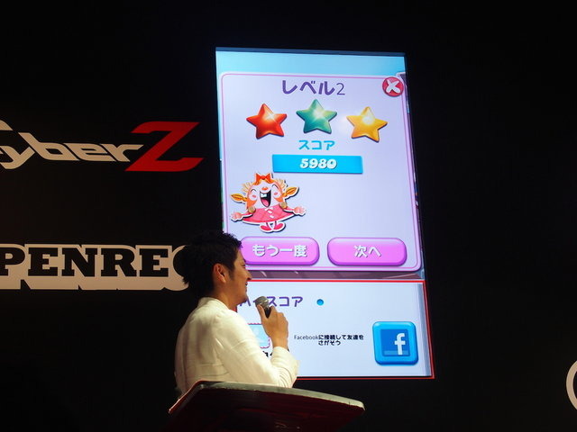 東京ゲームショウでCyberZはブースを出展し、スマホゲームプレイ動画共有サービス「OPENREC」のアピールを行いました。特設ステージではタレントの鈴木奈々さんを迎え、最近ハマっているという『キャンディクラッシュサーガ』のプレイ大会を開催。スタッフのサポートも