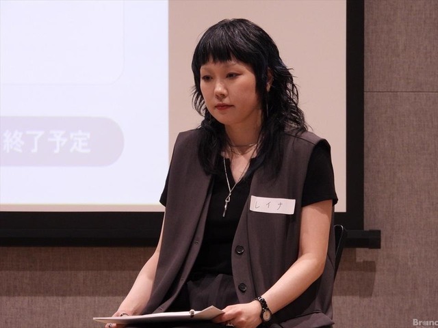 スクリーンの前に座り、膝元の手元の資料に視線を落としているREINAさん。『レイナ』という名札をつけた黒髪の人物